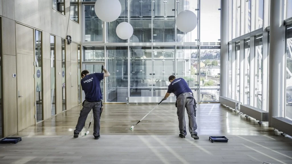 To personer påfører gulvbelegg i lyst, moderne kontorbygg.