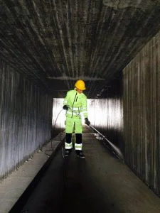 Person i verneutstyr høytrykkspyler vegger inne i betongtunnel.
