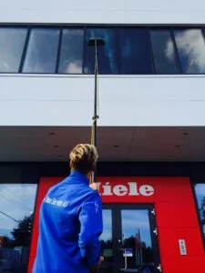 Person rengjør høyt vindu med langt skaft foran Miele inngang.