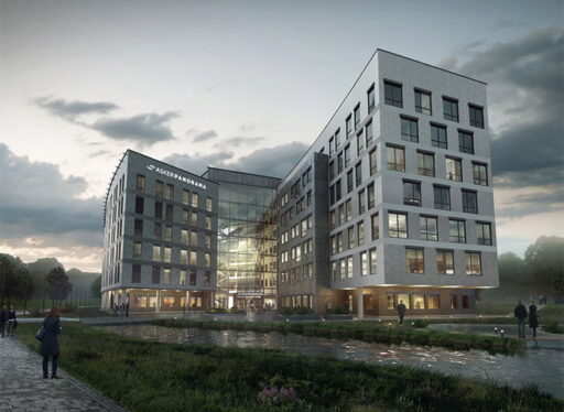 Moderne kontorbygg med glassfasade og grønt område foran.