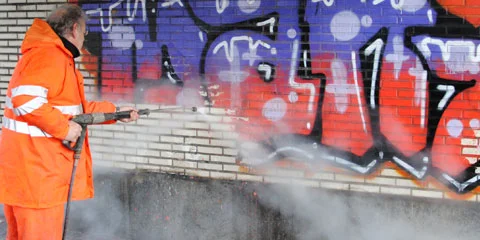 Graffiti fjernes fra murvegg med høytrykksspyler og damp.