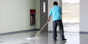 Person mopper blankt gulv foran heisdører og brannslukningsapparat.