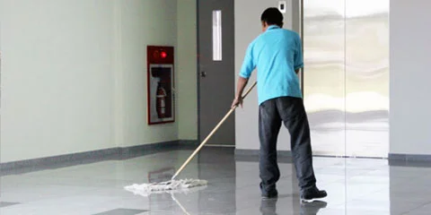 Person mopper blankt gulv foran heisdører og brannslukningsapparat.