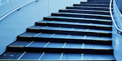 Mørke steintrapper med gule striper og metallrekkverk på begge sider.