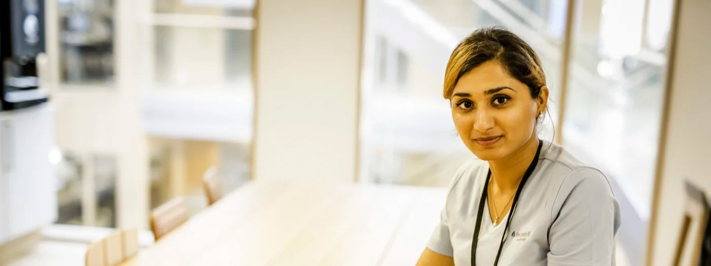 Person i arbeidsklær sitter ved bord i lyst rom.