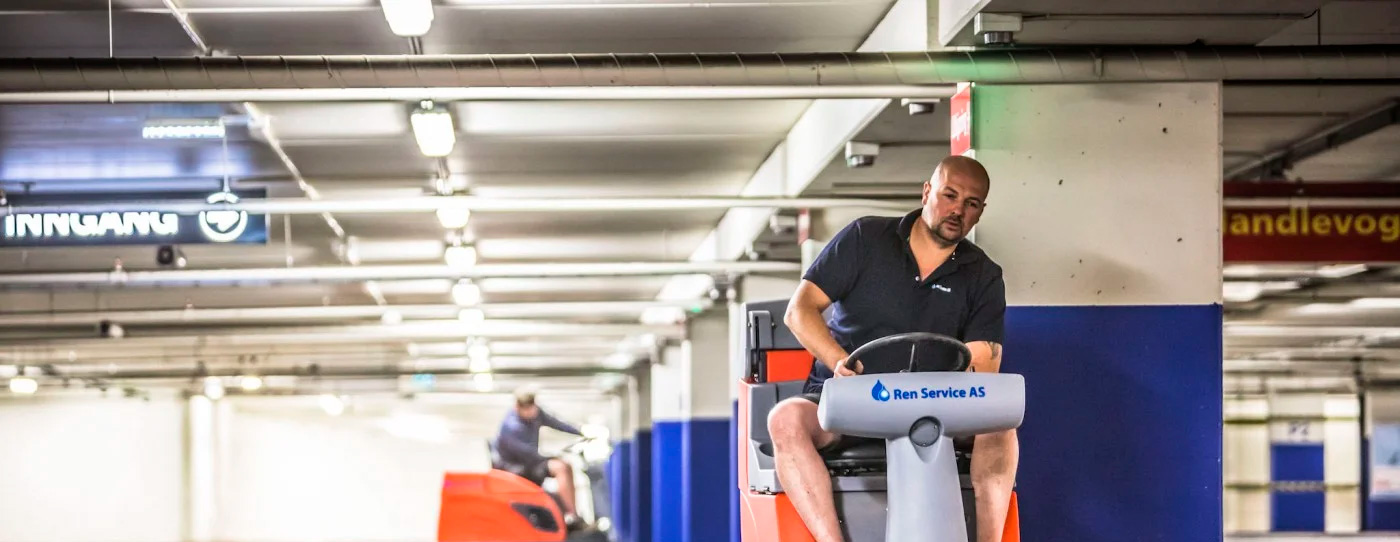 Gulvvaskemaskin rengjør betonggulv i parkeringshus med blå vegger.