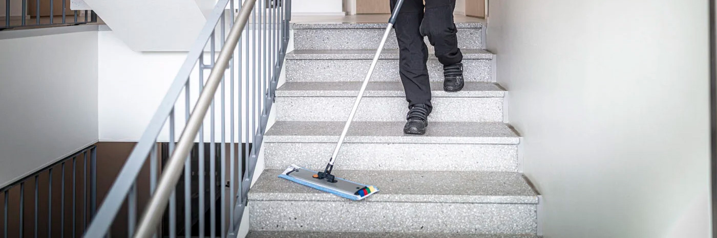 Person mopper trapp med flatt moppesystem i innendørs oppgang.