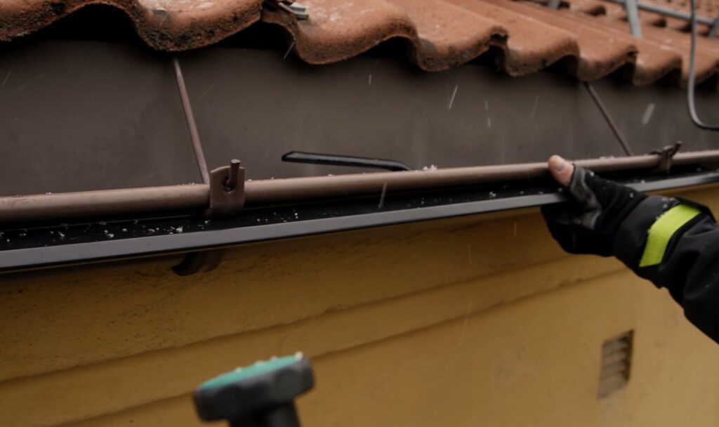 Person med hansker justerer en takrenne under et rødt tegltak